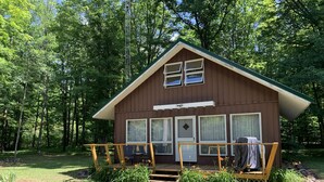 A small cabin with a porch, surrounded by a forest. - Muskegon River Cabin (Hersey)