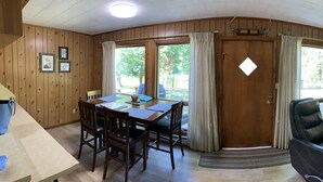 A wooden interior with a dining area, a sofa, and a door leading outside. - Muskegon River Cabin (Hersey)