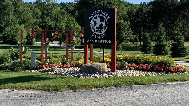 A sign for the Goldeneye Valley Association with a golf course in the background. - Muskegon River Cabin (Hersey)