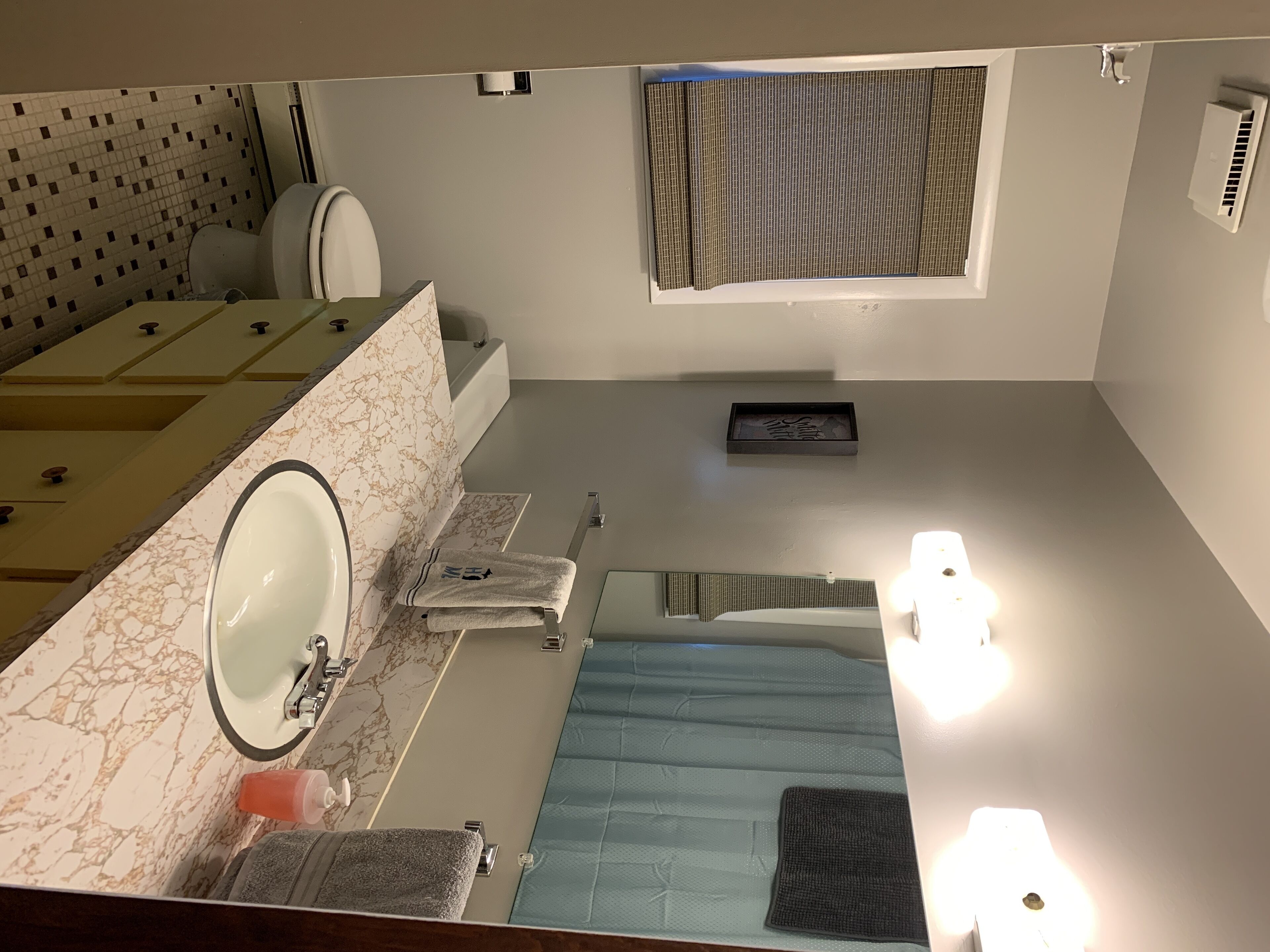 Ein kleines Badezimmer mit Marmorwaschtisch, Waschbecken, Toilette und Duschbereich.