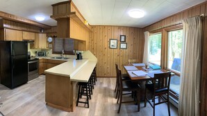 A kitchen with wooden cabinets, a black refrigerator, a microwave, and a dining area with a table and chairs. - Muskegon River Cabin (Hersey)