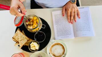 A person sitting at a table with a book, a glass of coffee, a jar of fruit, a plate with toast and butter, and a glass of smoothie.