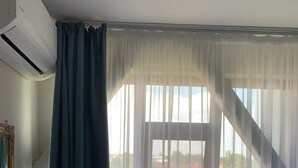 Una habitación con un ventanal grande, cortinas translúcidas y vistas a edificios.