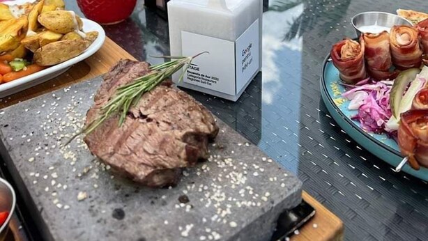 Una mesa de comedor con un bistec, papas asadas, una ensalada y una botella de bebida roja.