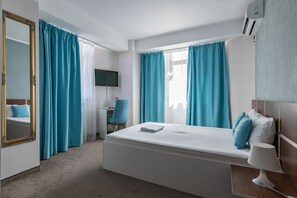 A hotel room with a bed, a desk, a chair, a TV, and a window with curtains. - Vila Bordeaux (Galati)