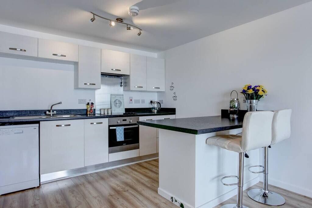 Une cuisine moderne avec des meubles blancs, un plan de travail noir et un tabouret de bar.