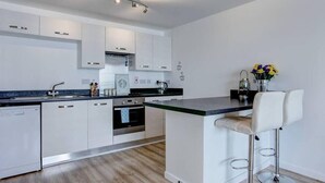 A modern kitchen with white cabinets, a black countertop, and a bar stool. - Clean and modern Riverside Flat w/ Private Balcony (Norwich)