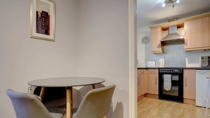 A compact kitchen with a round table and two chairs, wooden cabinets, a stove, and a dishwasher.