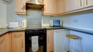 A compact kitchen with wooden cabinets, a stainless steel range hood, a microwave, a toaster, and a dishwasher.