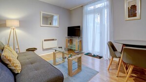 A modern living room with a sofa, a glass coffee table, a flat-screen TV, and a dining area with chairs.