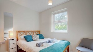A bedroom with a wooden bed, a nightstand, a chair, and a window with a view of greenery.