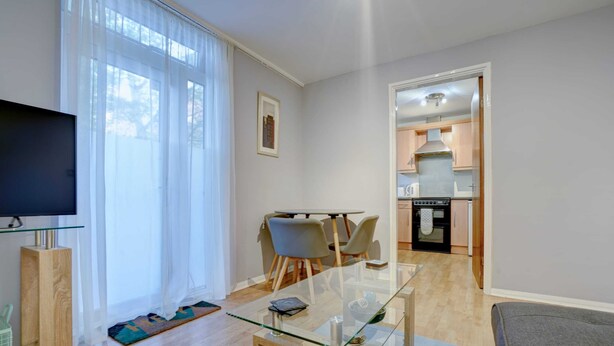 A modern living room with a glass coffee table, a flat-screen TV, and a dining area with chairs.