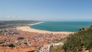 A coastal town with a beach, buildings with red roofs, and a clear blue sky. - Stunning View Apartment - Adults Only (Nazaré)