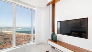 A modern living room with a large window offering a city view, a wooden console table, and a flat-screen TV. - Stunning View Apartment - Adults Only (Nazaré)