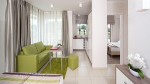 Un apartamento moderno con un sofá verde, una pequeña mesa de comedor, una zona de cocina y un dormitorio con cama.
