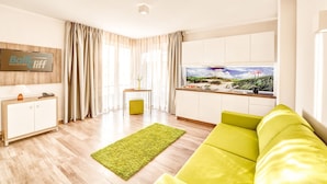 Una sala de estar moderna con un sofá verde, una pequeña cocina y un ventanal con vistas a la playa.