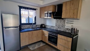 A compact kitchen with wooden cabinets, a stainless steel refrigerator, a microwave, and a built-in oven.