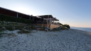 A beachside building with a wooden facade, a staircase leading to an upper level, and a view of the sea.