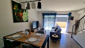 A dining area with a wooden table set for four, a television, and a sofa in the background.