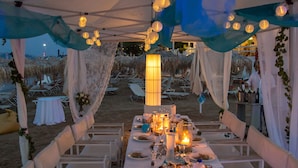 A beachside dining setup with white tables and chairs, candles, and a view of the beach. - Agistri Apartments (Agistri)