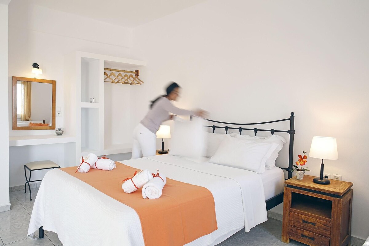 A neatly made bed with white and orange bedding, a bedside table with a lamp, and a mirror on the wall.