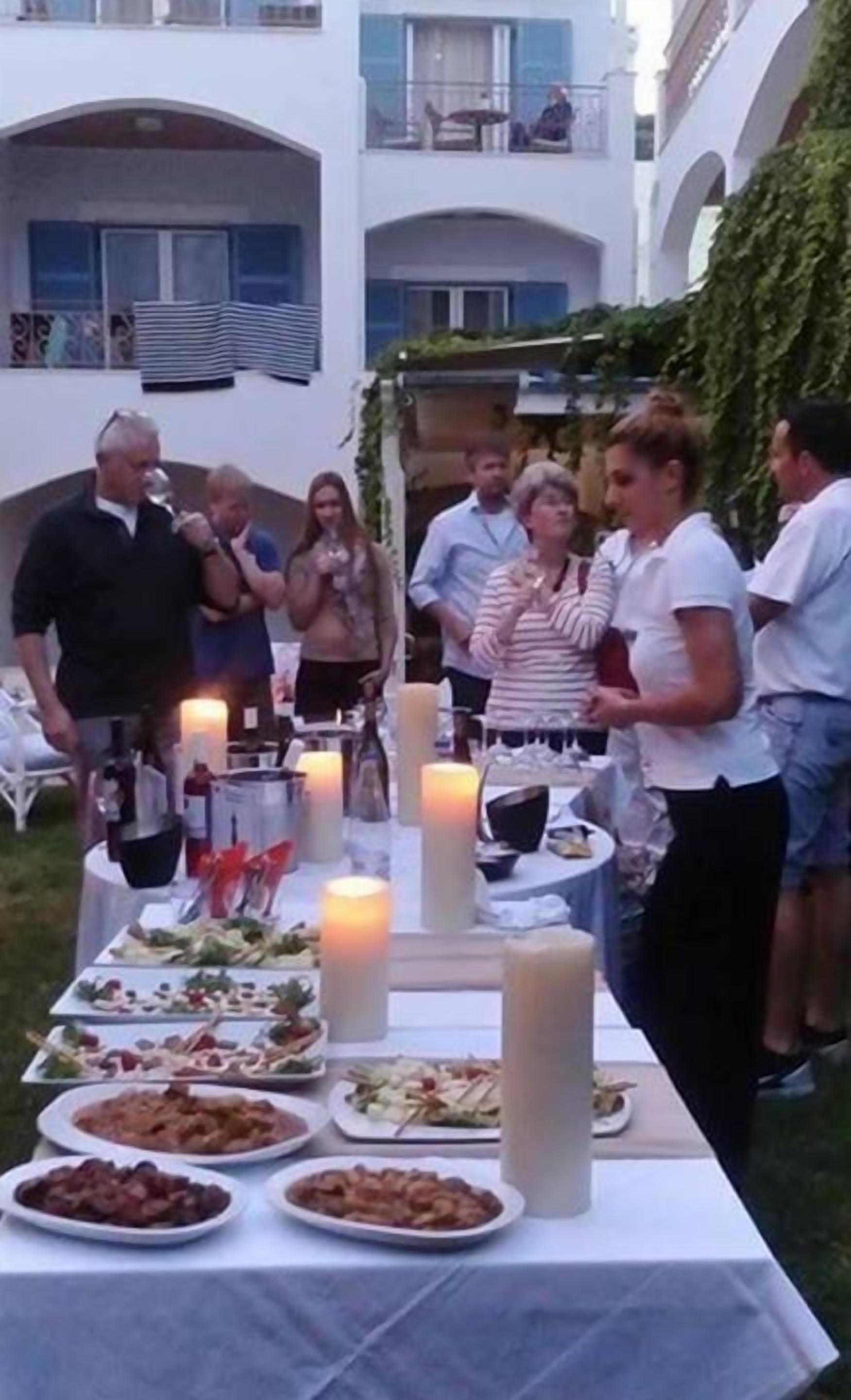 Un área de comedor al aire libre con mesas dispuestas para una comida, rodeada por un edificio blanco con balcones.