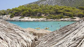 A beach with clear turquoise water, people swimming and on rafts, surrounded by rocky terrain and green trees.