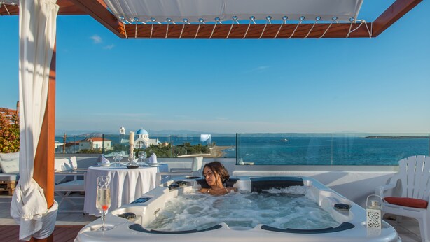 A person relaxing in a hot tub with a view of the sea and a coastal town. - Agistri Apartments (Agistri)