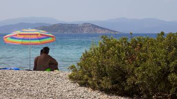 A beach with a person under a colorful umbrella, rocky terrain, and distant mountains.