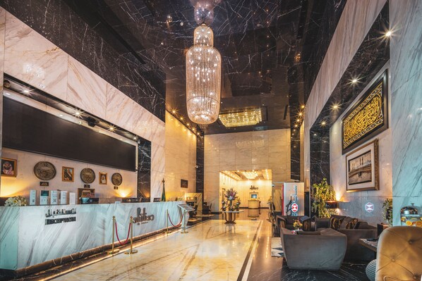 A lobby with a reception desk, a chandelier, marble walls, and a seating area.