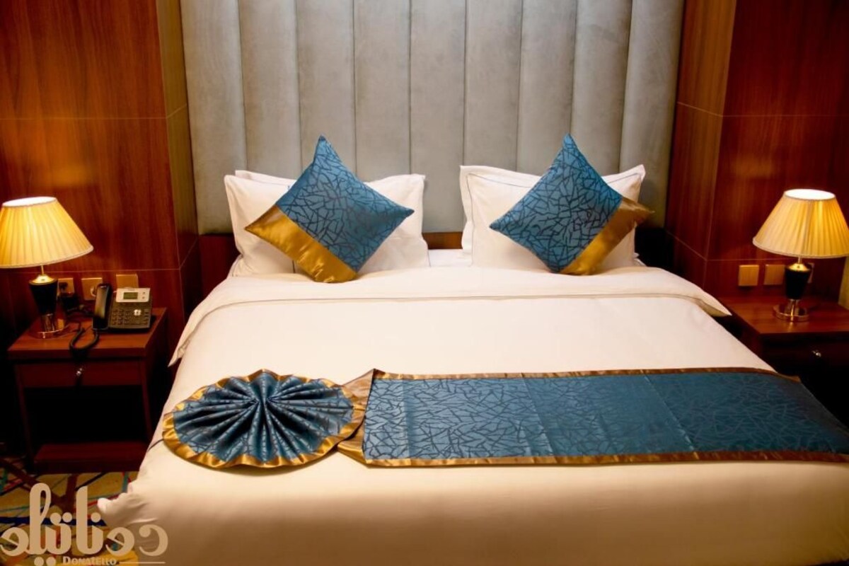 Una habitación de hotel con una cama, dos mesitas de noche y un cabecero.