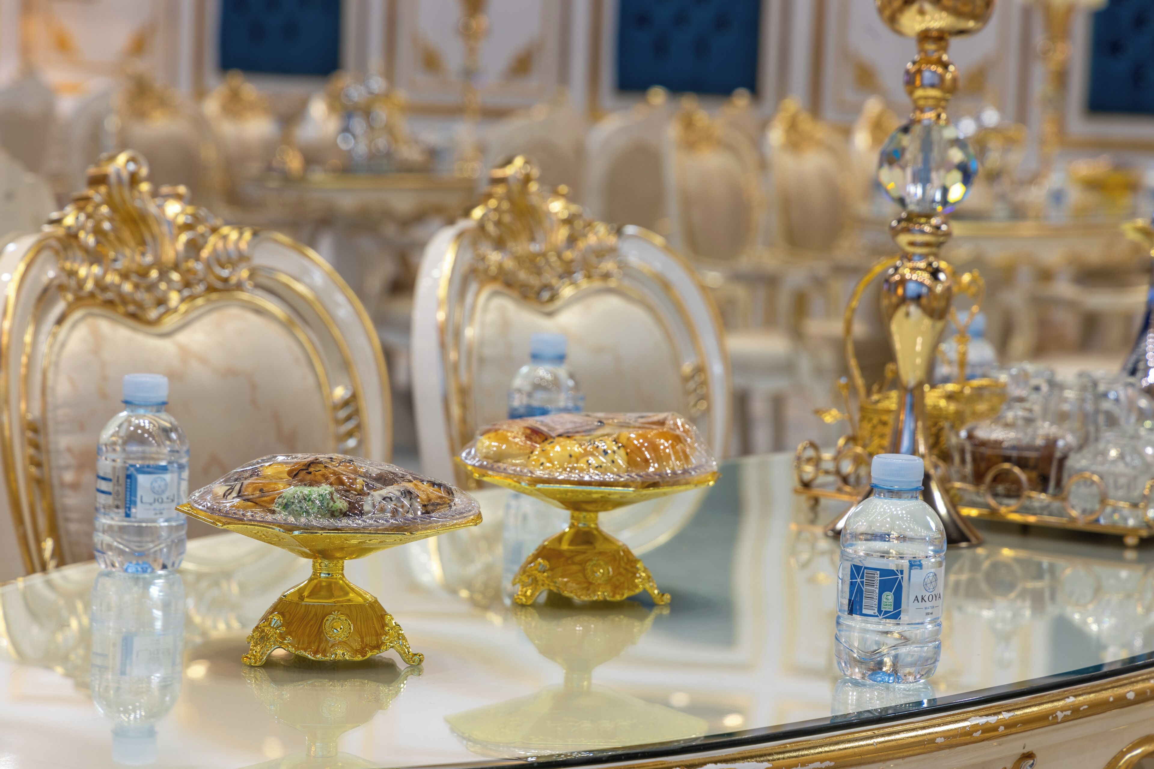 Une table à manger luxueuse, agrémentée de chaises dorées richement décorées, d’une bouteille d’eau et d’un présentoir en verre décoratif.