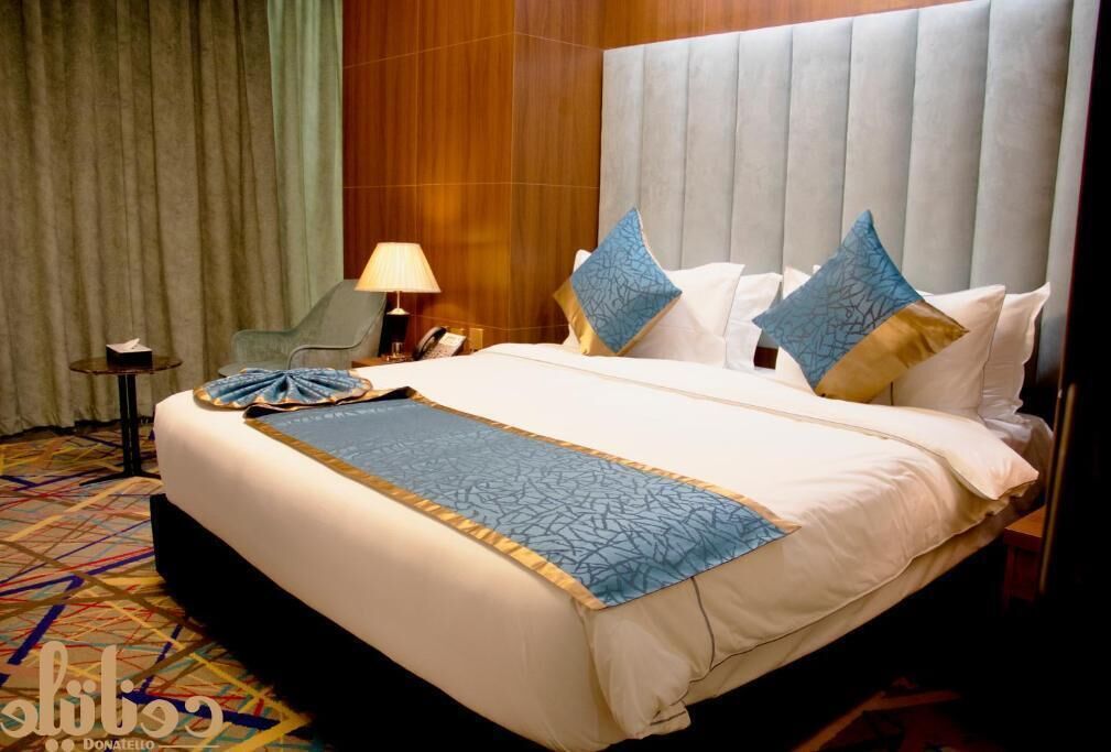 Una habitación de hotel con una cama grande, una mesita de noche, una lámpara y una silla.