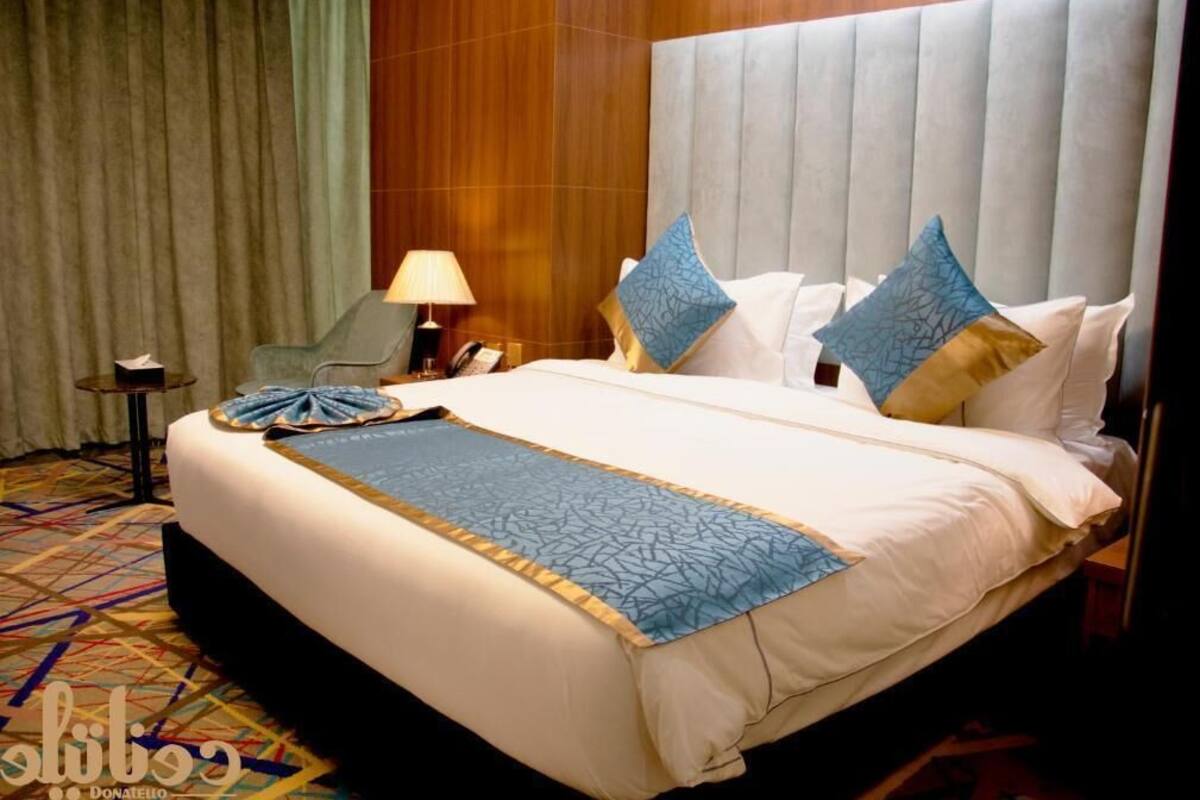 A hotel room with a large bed, a nightstand, a lamp, and a chair.