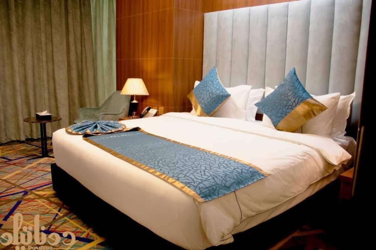 Una habitación de hotel con una cama grande, una mesita de noche, una lámpara y una silla.