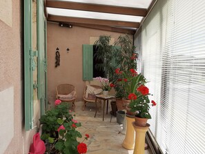 A covered outdoor area with wicker chairs, a table, and potted plants.