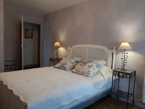 A neatly made bed with a white quilt, two floral pillows, and a white headboard. There are two bedside tables with lamps, one on each side of the bed. - Gîte "château les Cèdres" 4 Pers. 90 m2, au Coeur du Vignoble (BERSON)