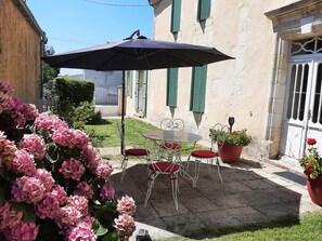 En terrasse med et bord, stole, en stor parasol og plantekrukker.