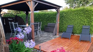 An outdoor patio with a wooden deck, seating area, and potted plants.