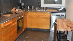 A modern kitchen with wooden cabinets, a black countertop, a built-in oven, a coffee maker, and a window with a view of trees.