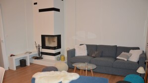 A modern living room with a fireplace, grey sofa, blue ottoman, and round coffee table.