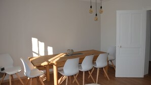 A dining area with a wooden table and white chairs, a white door, and a hanging light fixture.