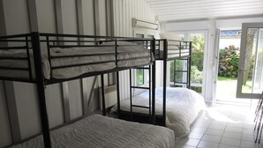 Une chambre de dortoir avec des lits superposés, une fenêtre et une porte donnant sur un balcon.
