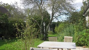 Un espace extérieur aménagé avec une table et des bancs, entouré de verdure et d’arbres.