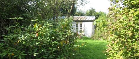 A white building with a metal roof, surrounded by dense greenery and trees.