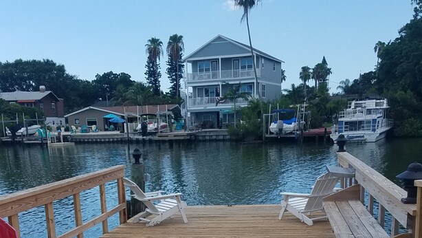 Eine Holzterrasse mit Stühlen, Blick auf ein Haus und Boote auf dem Wasser.
