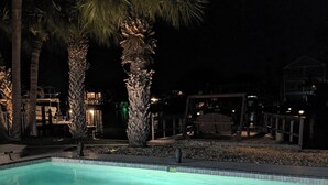 Ein Schwimmbecken bei Nacht mit klarem Wasser, umgeben von Palmen und einer Liegefläche mit Sitzgelegenheiten.