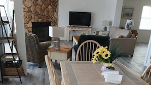 Ein Essbereich mit Tisch, Stühlen, einer Blumenvase und einem Fernseher im Hintergrund.