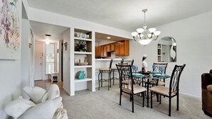 A dining area with a round table, black chairs, and a chandelier. There are shelves with decorative items and a white sofa in the foreground. - Runaway Bay 213 - 1845191 (Bradenton Beach)