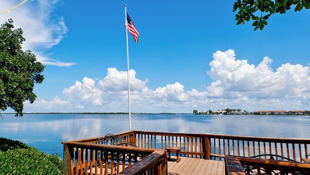 A wooden deck with a flagpole, a bench, and a table. - Runaway Bay 213 - 1845191 (Bradenton Beach)